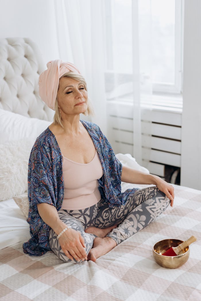 Senior woman in peaceful meditation with a Tibetan singing bowl on bed, embracing a tranquil lifestyle.